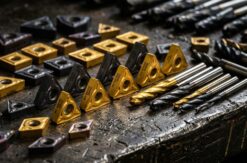 Macro array of carbide milling inserts and end mills laid on dark steel, gold titanium nitride and gunmetal coatings...