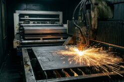 Fiber laser cutting head tracking through sheet steel, brilliant cut point and a fan of sparks, automated sheet loader...